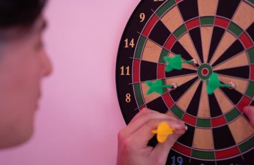 A person focusing on adjusting darts on a dartboard, symbolizing precision and leisure.